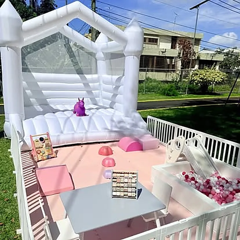 Bounce house blanco con paneles transparentes y área de soft play rosa en el patio